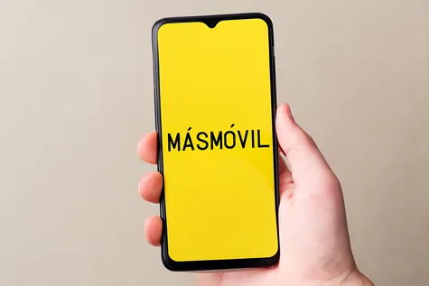 Mano sosteniendo móvil con pantalla amarilla y texto “MÁSMÓVIL” centrado.