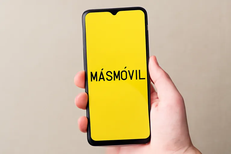 Mano sosteniendo móvil con pantalla amarilla y texto “MÁSMÓVIL” centrado.