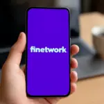 Mano sosteniendo móvil con fondo morado y la palabra "Finetwork" en blanco centrada en pantalla