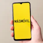 Mano sosteniendo móvil con pantalla amarilla y texto “MÁSMÓVIL” centrado.